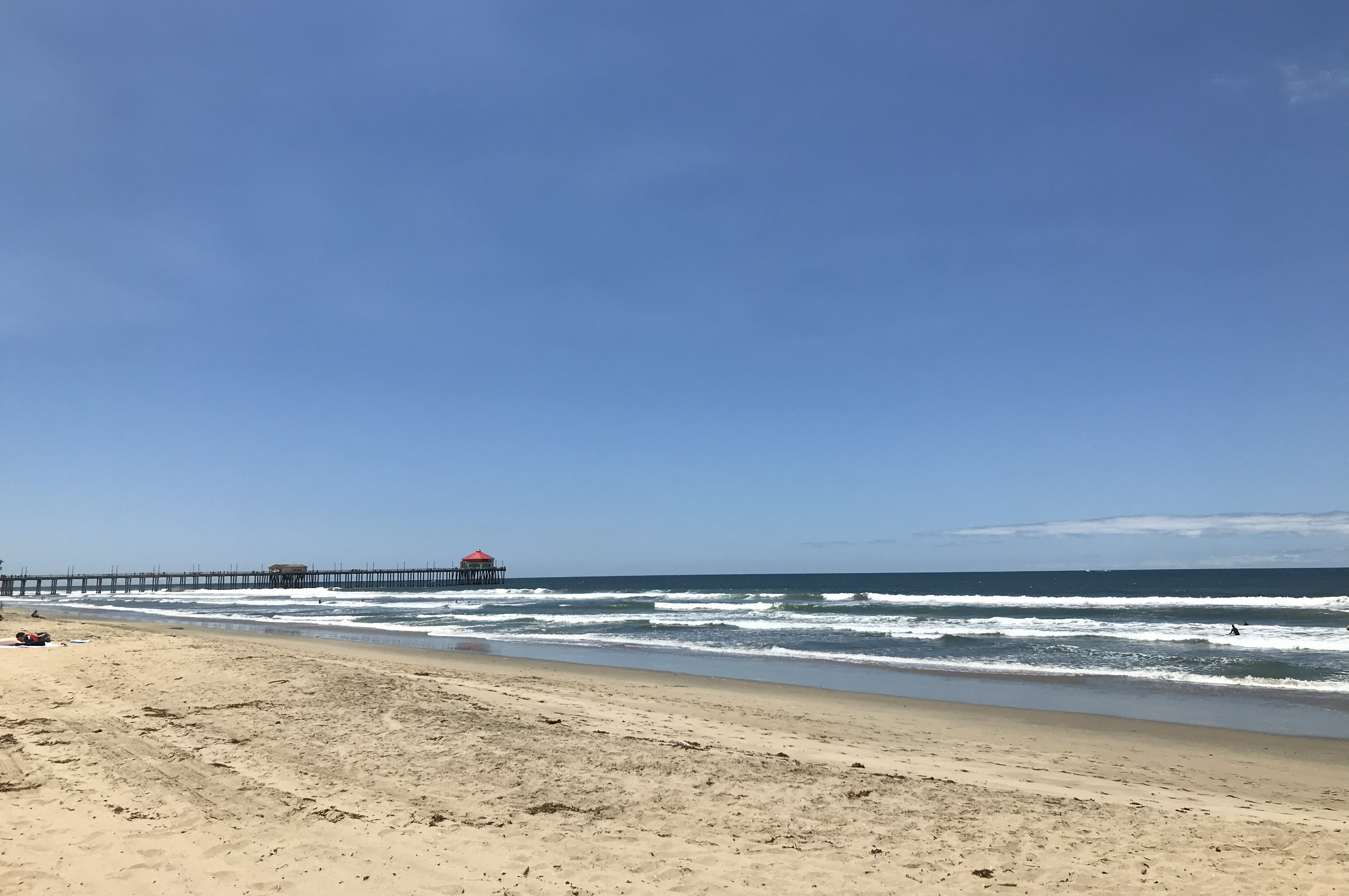 Sandy beach, pier, breaking waves under a blue sky