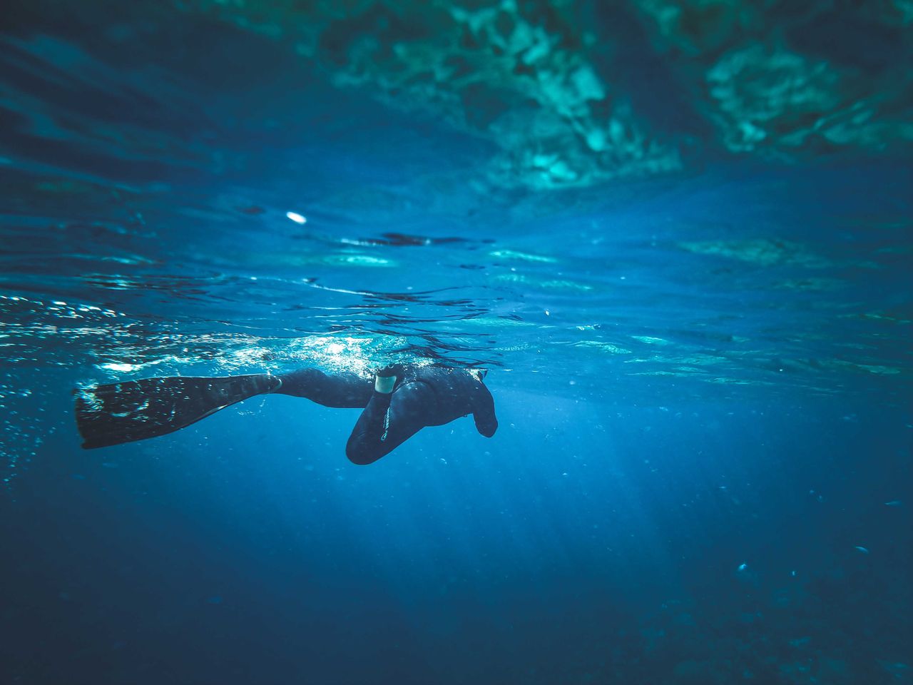 Diver in fins under the water with sun shining through blue water